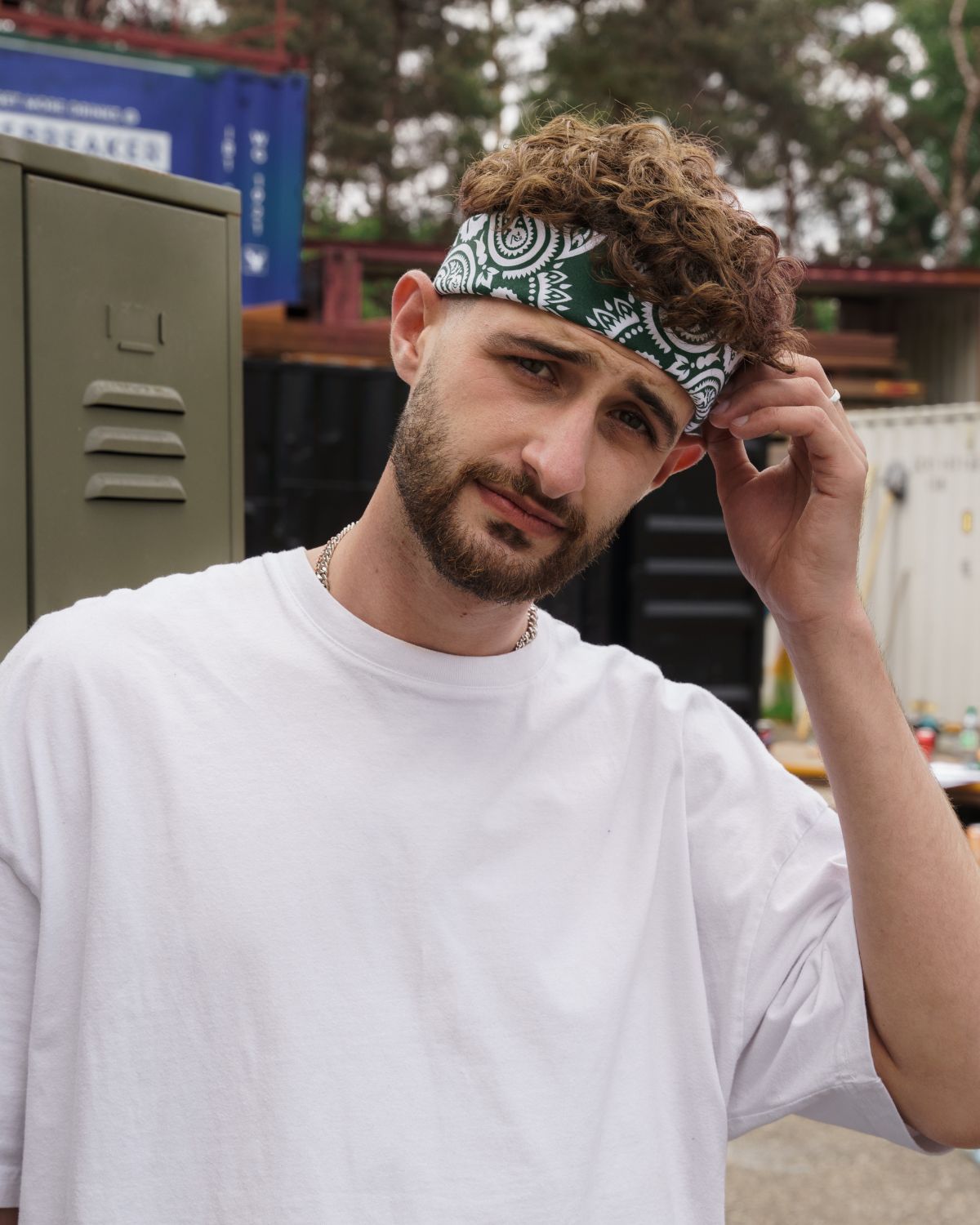 (DE) Ein Mann trägt eine dunkelgrüne Bandana it weißem Blumenmuster um seine Stirn gewickelt. (EN) A man wears a dark green bandana with a white floral pattern wrapped around his forehead.