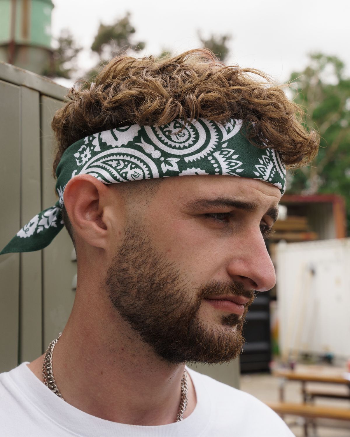 (DE) Ein Mann trägt eine dunkelgrüne Bandana it weißem Blumenmuster um seine Stirn gewickelt. (EN) A man wears a dark green bandana with a white floral pattern wrapped around his forehead.
