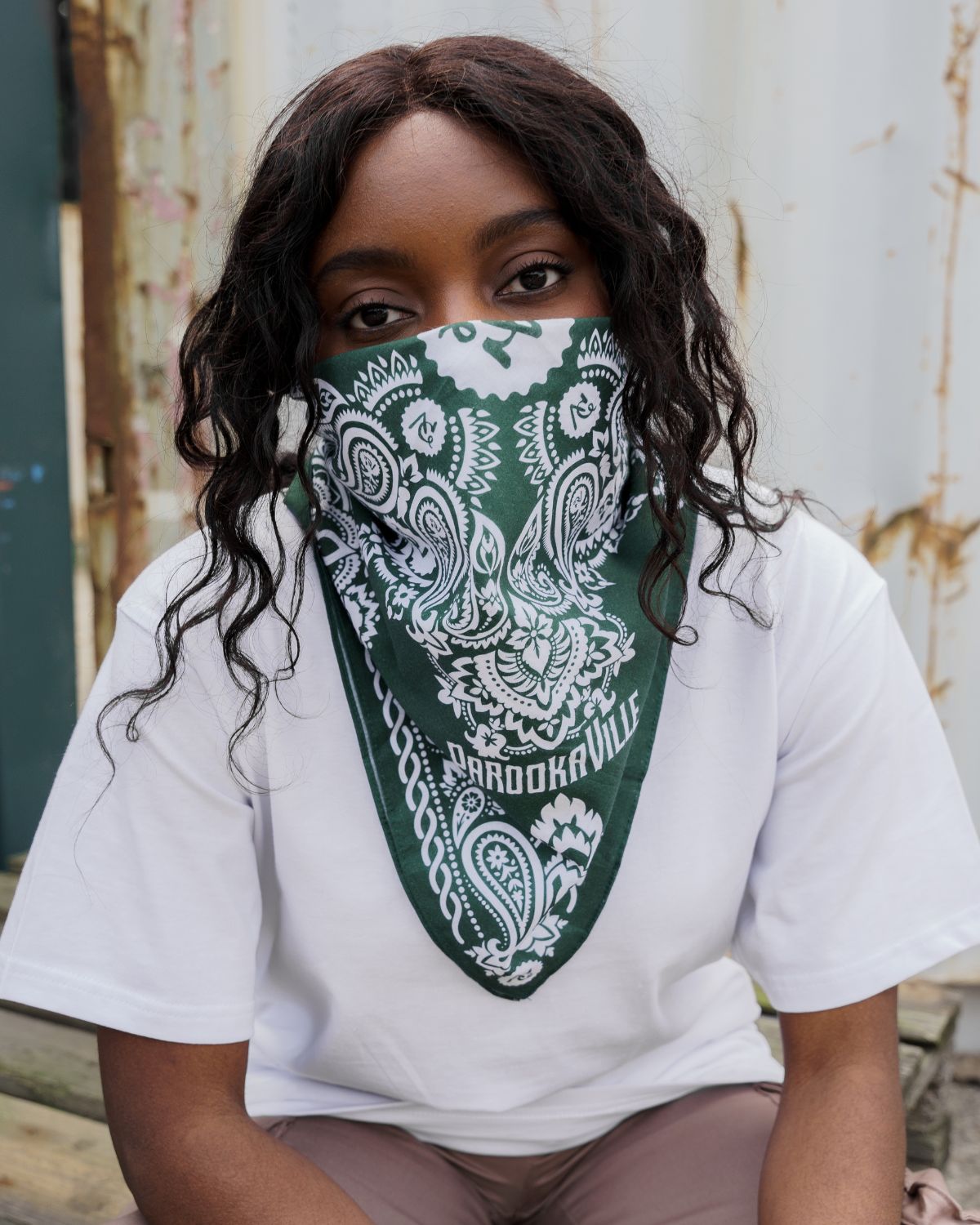 (DE) Eine Frau trägt ein weißes T-Shirt und eine dunkelgrüne Bandana mit weißem PAROOKAVILLE Schriftzug und weißen Blumenmuster. (EN) A woman is wearing a white T-shirt and a dark green bandana with white PAROOKAVILLE lettering and a white floral pattern.