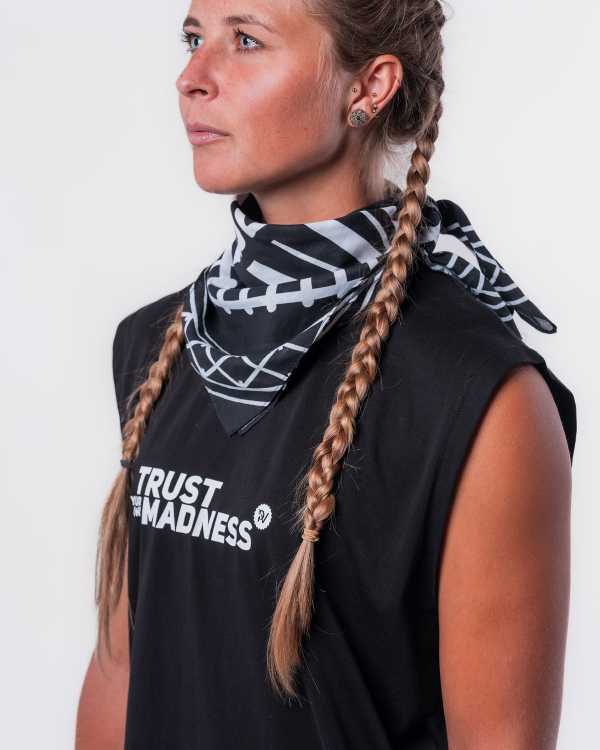 (DE) Eine Frau trägt die Bandana mit Rails Motiv um den Hals und dazu das schwarze MuskelShirt "TRUST YOUR OWN MADNESS". (EN) A woman wears the bandana with rails motif around her neck and the black muscle shirt ‘TRUST YOUR OWN MADNESS’.