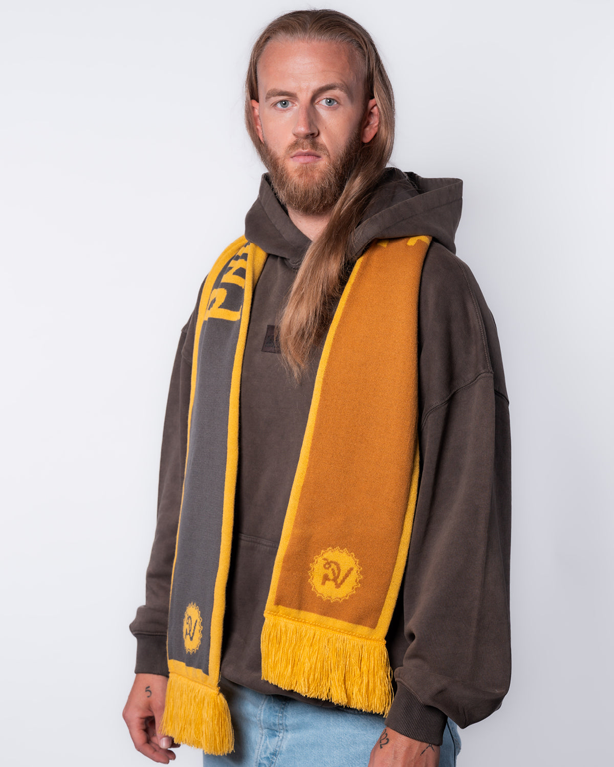 (DE) Man sieht eine Person, die den wendbaren PV Fan Schal trägt. Die unterschiedlichen Seiten trägt sie jeweils über eine Schulter: Eine Seite ist gold-gelb, die andere grau-gelb. (EN) One can see a person that is wearing a reversible PV fan scarf. They carry the different sides over each shoulder: One side it gold-yellow and the other is grey-yellow.