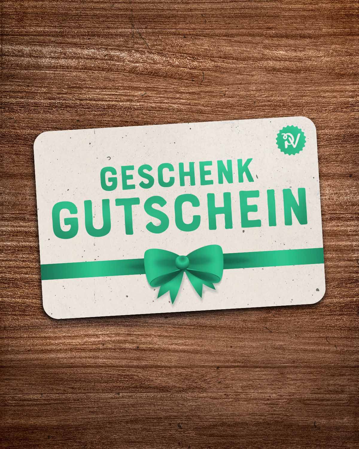 (DE) Man sieht einen beigefarbenen Geschenkgutschein mit einer grünen Aufschrift und einer grünen Schleife. (EN) One can see a beige gift voucher with a green bow and green inscription.