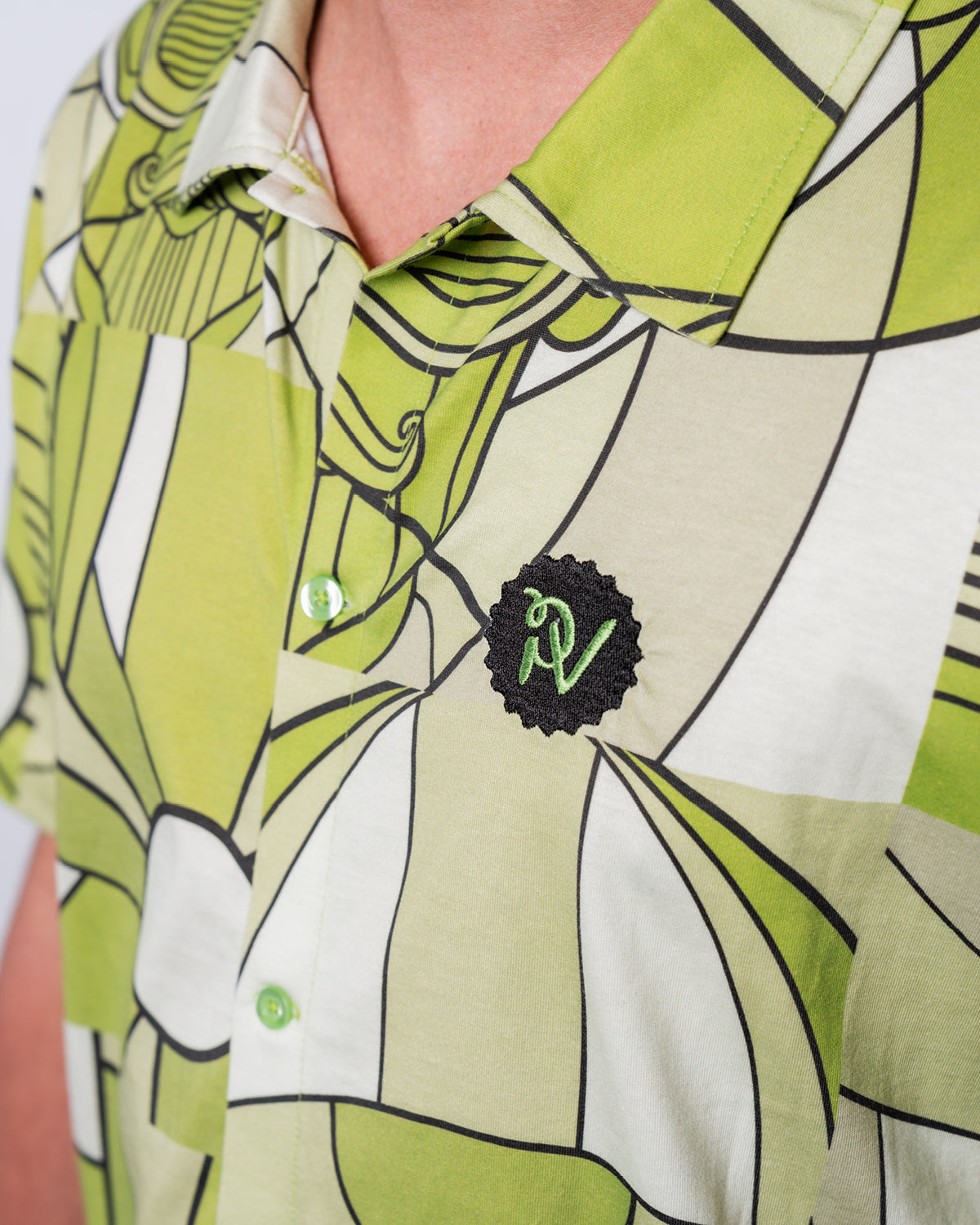 (DE) Man sieht eine Nahansicht des Hemdes mit Bill-Print. Rechts oben ist das PV Emblem in grün auf schwarzem Untergrund aufgestickt. (EN) One can see a close-up view of the Bill Print shirt. On the right top corner there is a green PV emblem embroided on a black base.