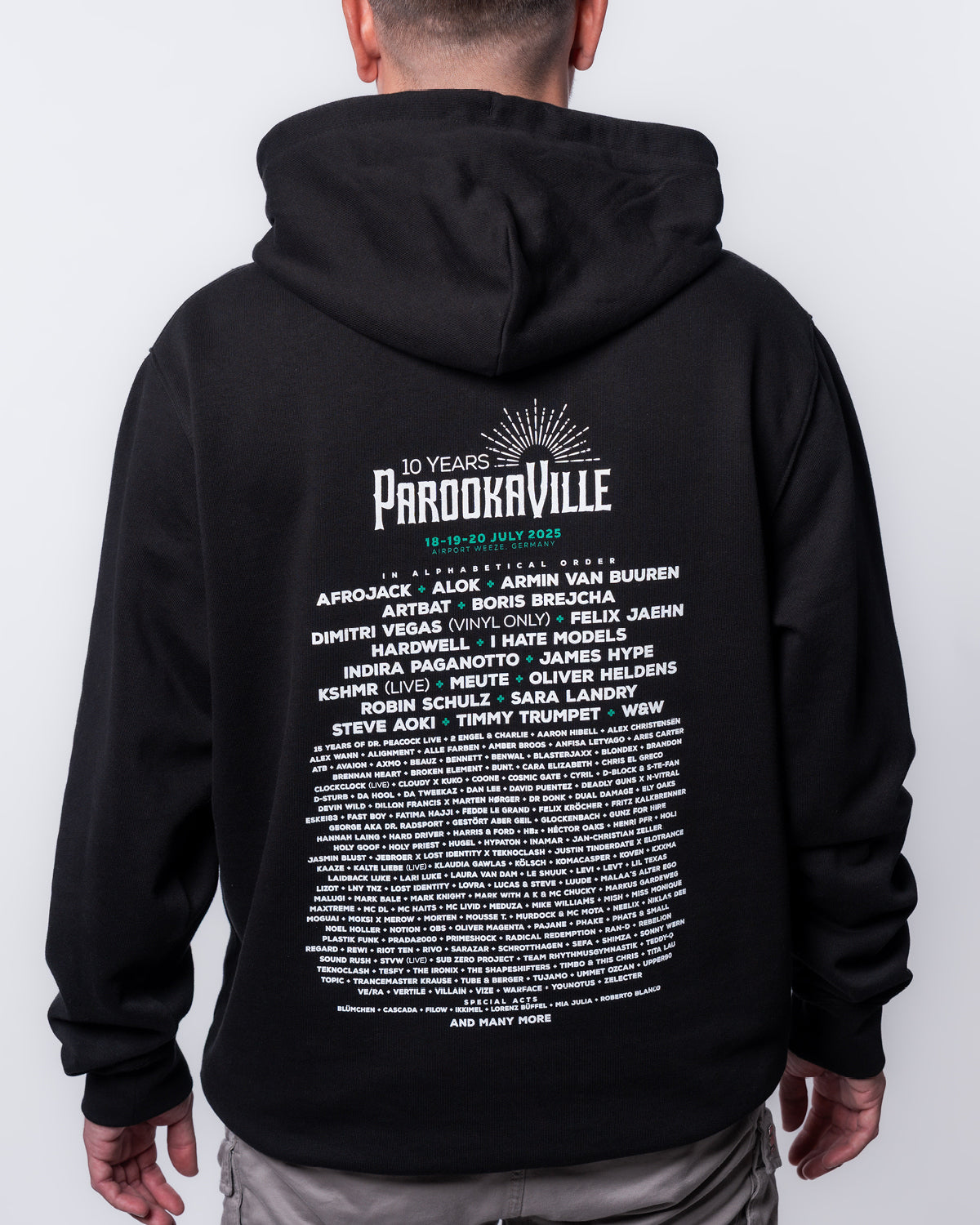 (DE) Ein Mann trägt den schwarzen Line-Up Hoodie. Auf der Rückseite stehen die Artists unter dem 10 Years PAROOKAVILLE Logo aufgelistet. (EN) A man wears the black line-up hoodie. The artists are listed on the back under the 10 Years PAROOKAVILLE logo.