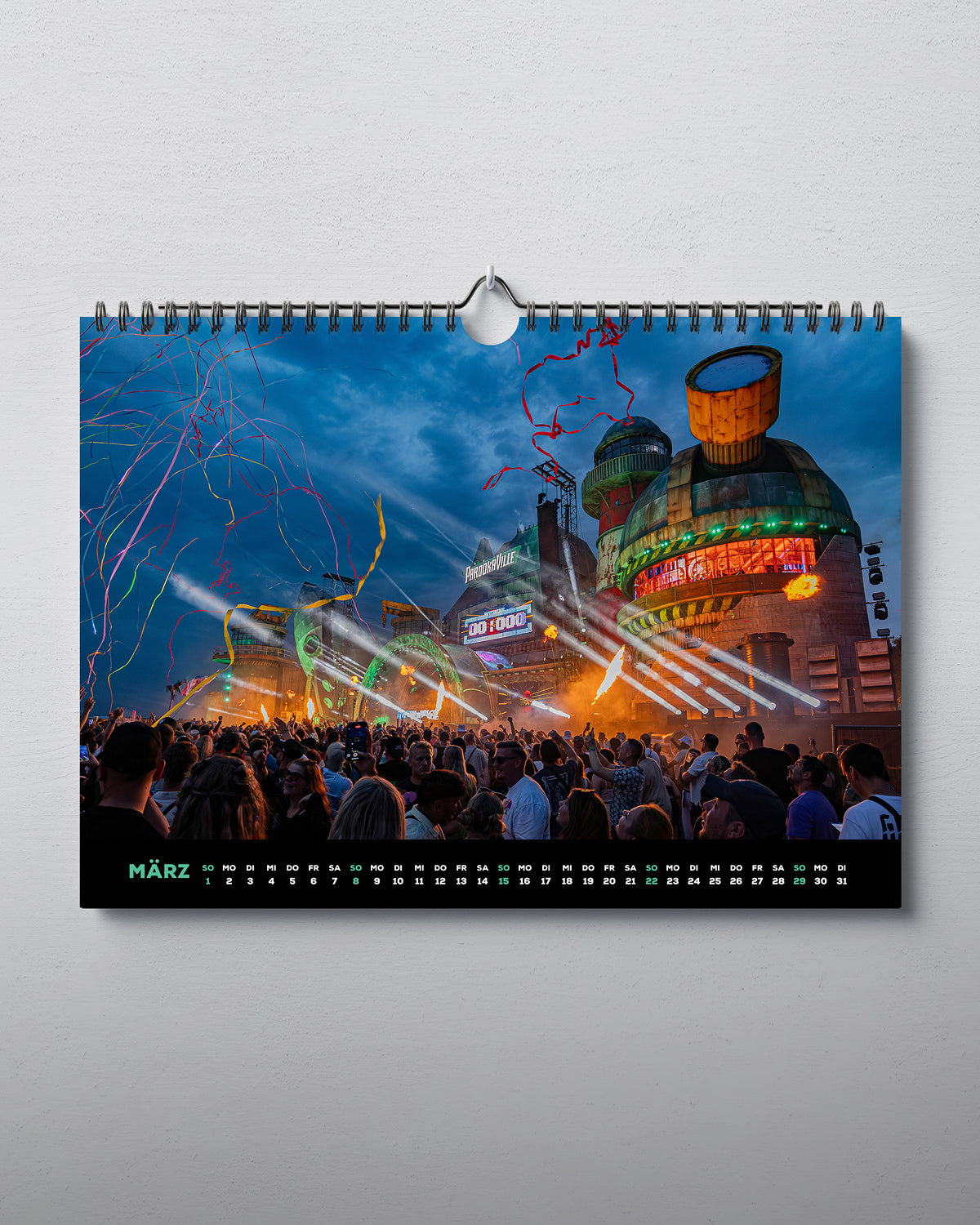 Zu sehen ist der März des horizontal aufhängbaren Kalenders. Mittig abgedruckt ist die New Bills Factory aus 2025. Unten dem Bild ist ein Streifen mit den Tagen und Wochenenden des Monats.