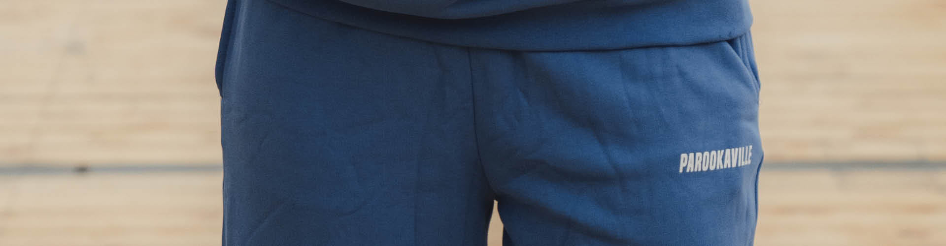 (DE) Man sieht eine Nahansicht der blauen Jogginghose. Auf der rechten Seite trägt diese unter der Hosentasche den weißen Schriftzug "PAROOKAVILLE". (EN) One can see a close-up view of the blue sweat pants. At the top side of the right trouser leg is the white inscription "PAROOKAVILLE".
