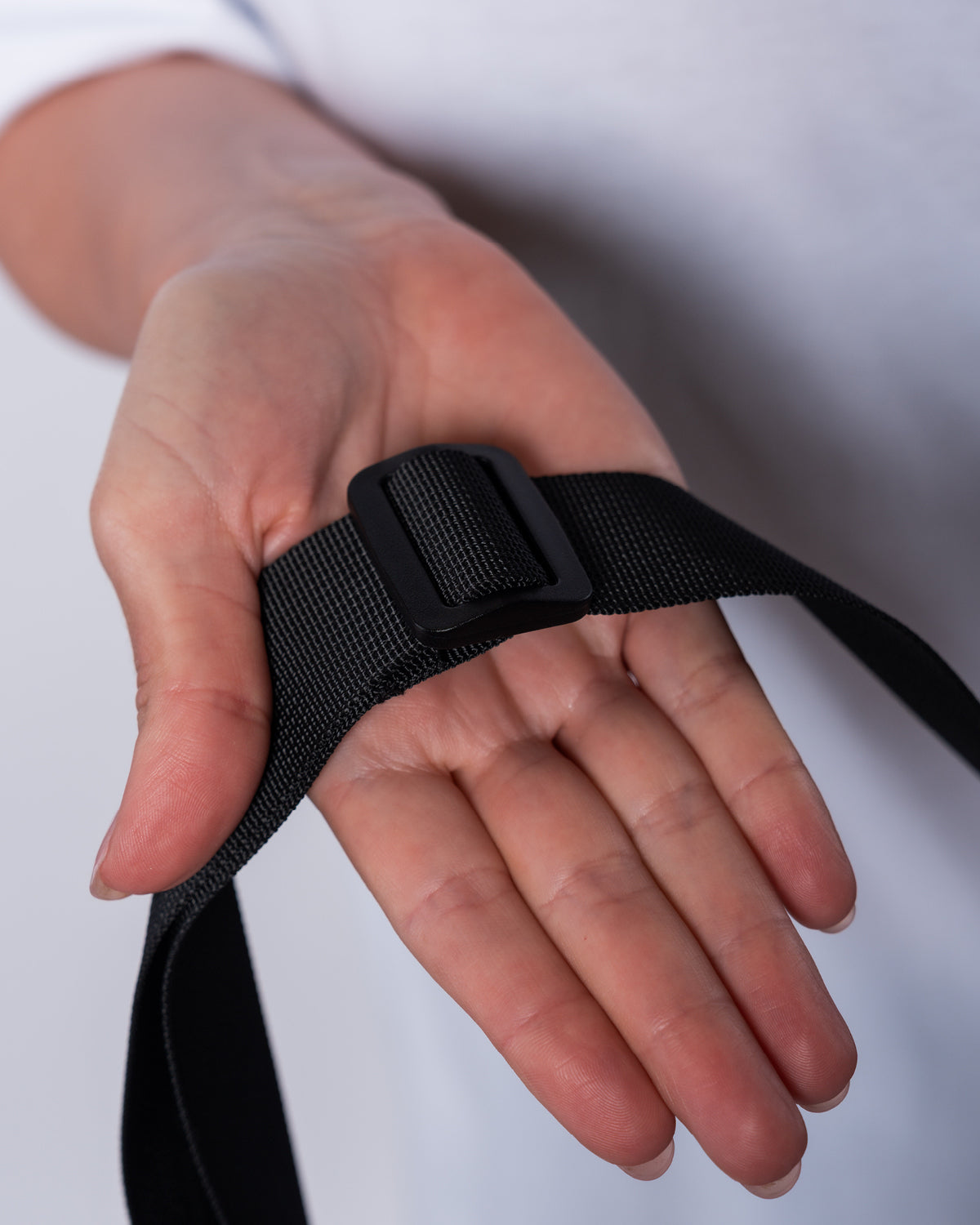 (DE) Man sieht die Nahansicht einer ausgestreckten Hand, die den Gurt der Leo Moonbag hält. Man erkennt die schwarze Schnalle mit welcher der Gurt verstellt werden kann. (EN) One can see a close-up view of a hand holding the strap of the Leo Moonbag. The observer can recognize the black buckle at the strap, which can be used to adjust the strap.