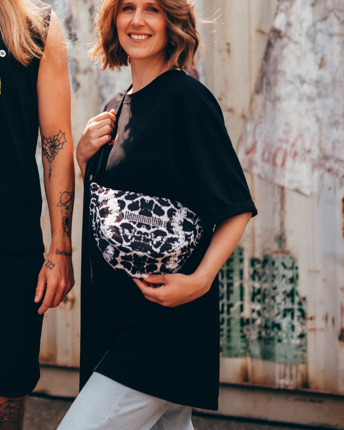(DE) Eine Frau trägt die PAROOKAVILLE Moonbag. Die Tasche ist schwarz-weiß gefleckt. (EN) A woman carries the PAROOKAVILLE Moonbag. The bag is spotted in black and white.