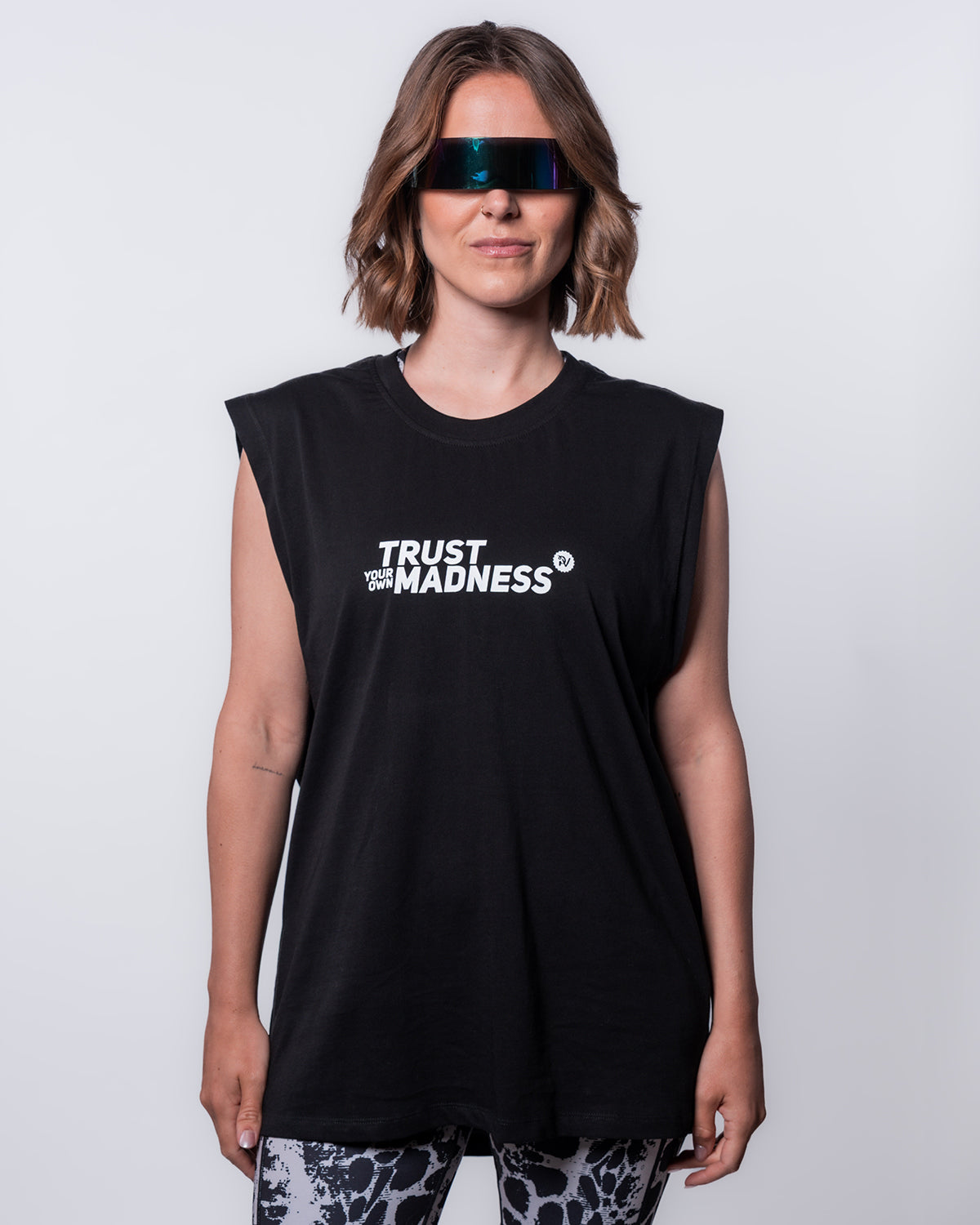 (DE) Eine Frau trägt das Muskelshirt "Madness" mit der weißen Aufschrift "TRUST YOUR OWN MADNESS" und dazu die Shield Sonnenbrille. (EN) A woman wears the muscle shirt "Madness" with the white inscription "TRUST YOUR OWN MADNESS" and the Shield sunglasses.