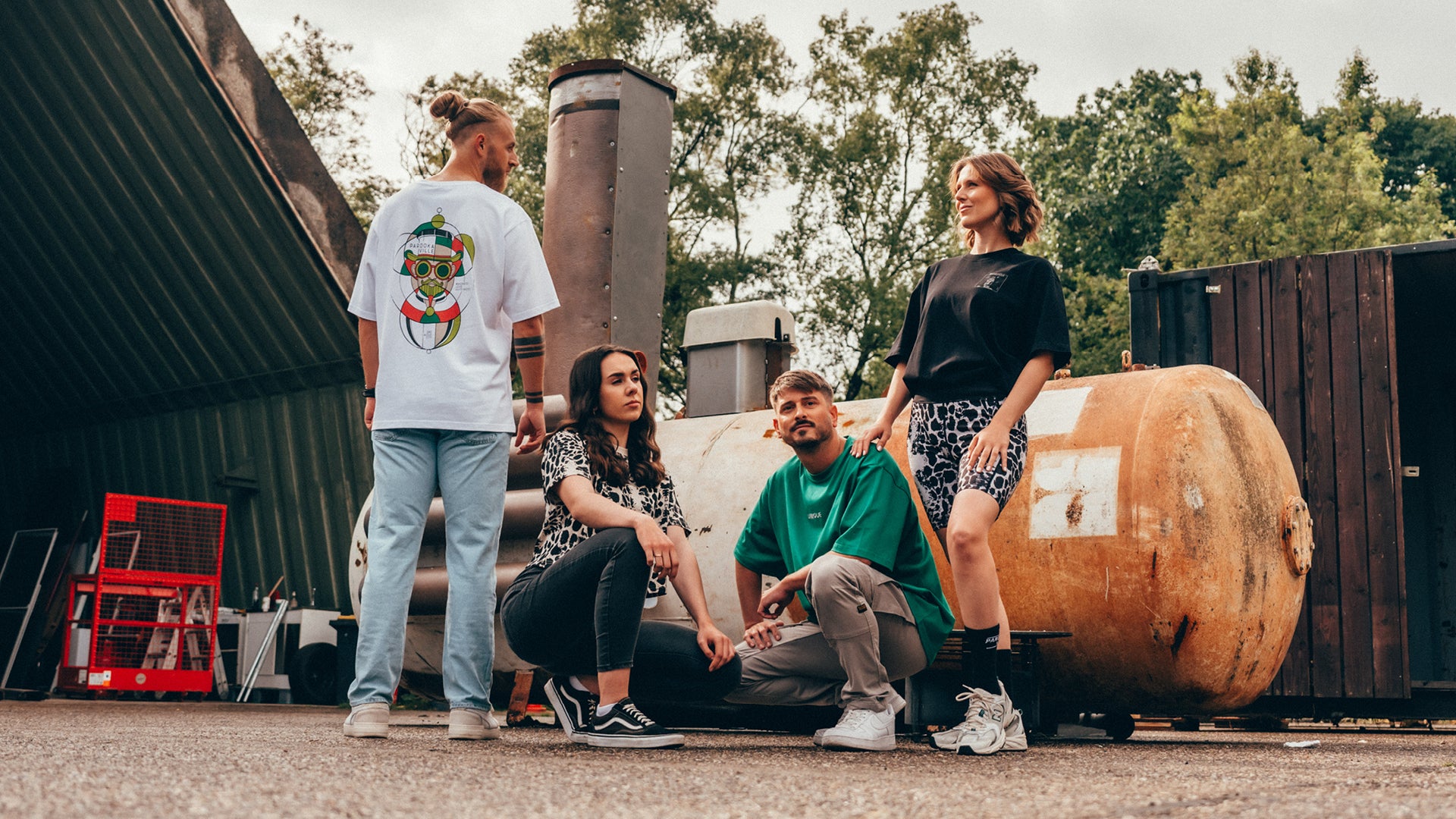 (DE) Vier Personen tragen die Street Style Kollektion. Der Mann links trägt das Bill-In-Circles T-Shirt, der Mann in der Mitte trägt ein grünes s T-Shirt und die beiden Frauen tragen Kleidungsstücke mit Leopardenmuster. (EN) Four people are wearing the Street Style collection. The man on the left is wearing the Bill In Circles T-shirt, the man in the centre is wearing a green s T-shirt and the two women are wearing leopard print garments.
