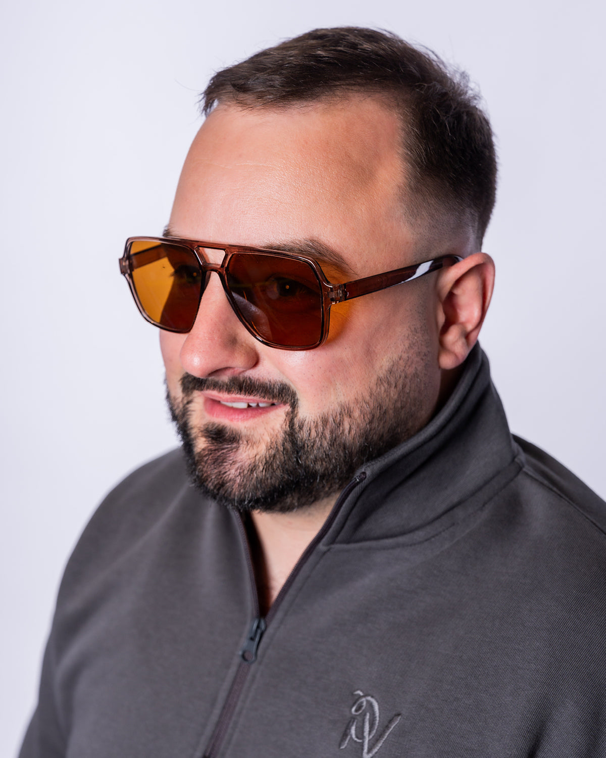 Ein Mann trägt die Urban Aviator Sonnenbrille mit eckigen, braun getönten Gläsern, einem transparent braunen Rahmen und markantem Doppelsteg. Die Nahaufnahme hebt das moderne Aviator-Design und die klaren Linien der Brille vor hellem Hintergrund hervor.