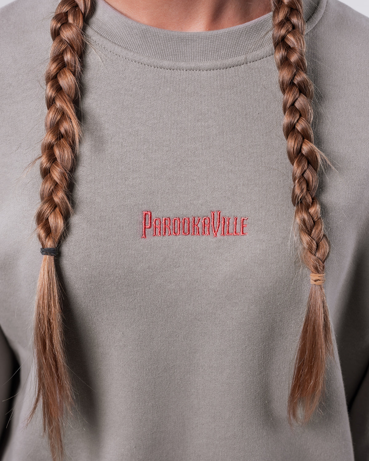 (DE) Man sieht eine Nahansicht des grauen Heart Sweaters. Dort ist vorne der Schriftzug "PAROOKAVILLE" in großen, roten Buchstaben aufgestickt. (EN) One can see a close-up view of the grey Heart Sweater. There is the bold red inscription "PAROOKAVILLE" embroided at the front.