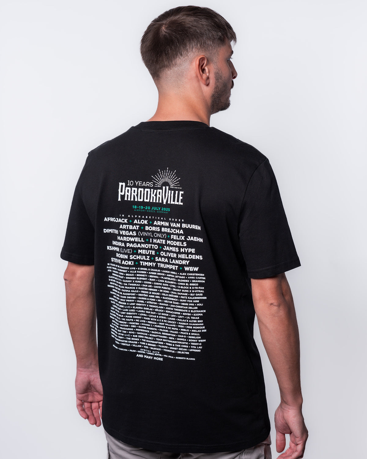 (DE) Ein Mann trägt das schwarze Line-Up T-Shirt. Auf dem Backprint steht in weißer Schrift das 10 Years PAROOKAVILLE- Schriftemblem und die Künstler. Die Festivaldaten sind grün. (EN) A man is wearing the black line-up T-shirt. The 10 Years PAROOKAVILLE logo and the artists are written in white on the back print. The festival dates are in green.