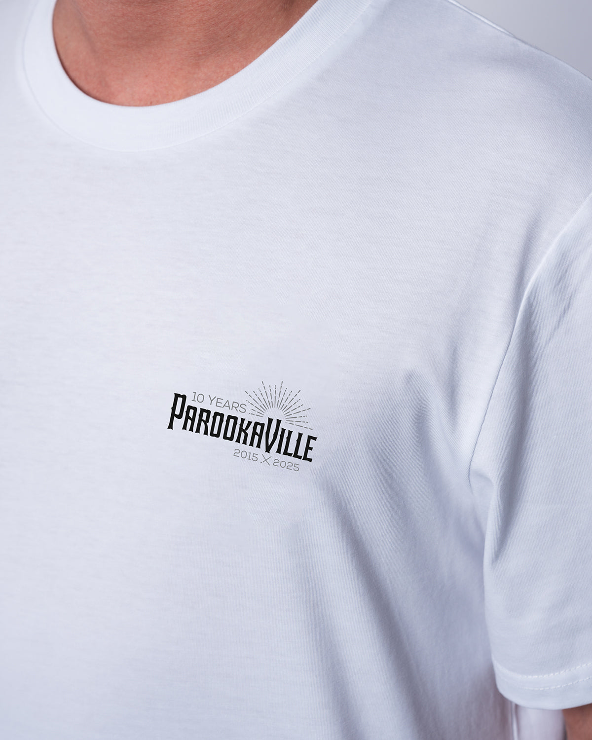 (DE) Man sieht eine Nahansicht des weißen T-Shirts mit dem schwarzen 10 Years PAROOKAVILLE Schriftzug auf der rechten Oberseite. (EN) You can see a close-up view of the white T-shirt with the black 10 Years PAROOKAVILLE lettering on the top right.