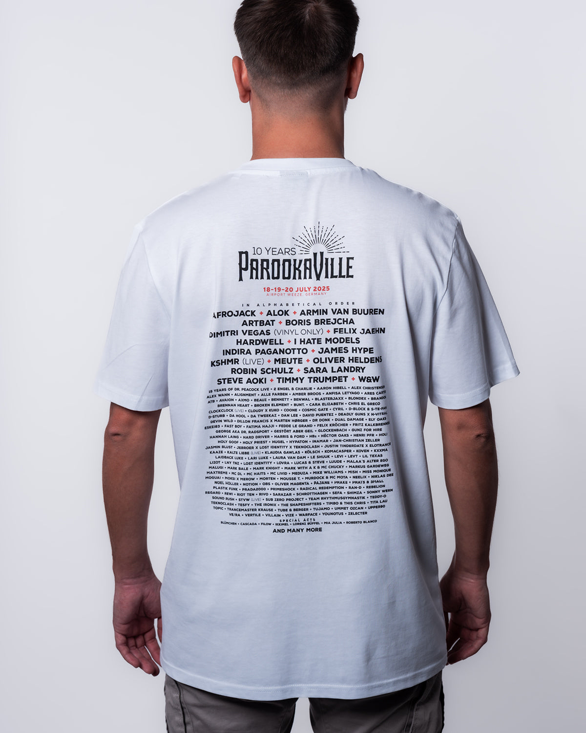(DE) Ein Mann trägt ein weißes T-Shirt mit Line-Up Backprint und dem 10 YEARS PAROOKAVILLE Logo. (EN) A man wears a white T-shirt with a line-up backprint and the 10 YEARS PAROOKAVILLE logo.