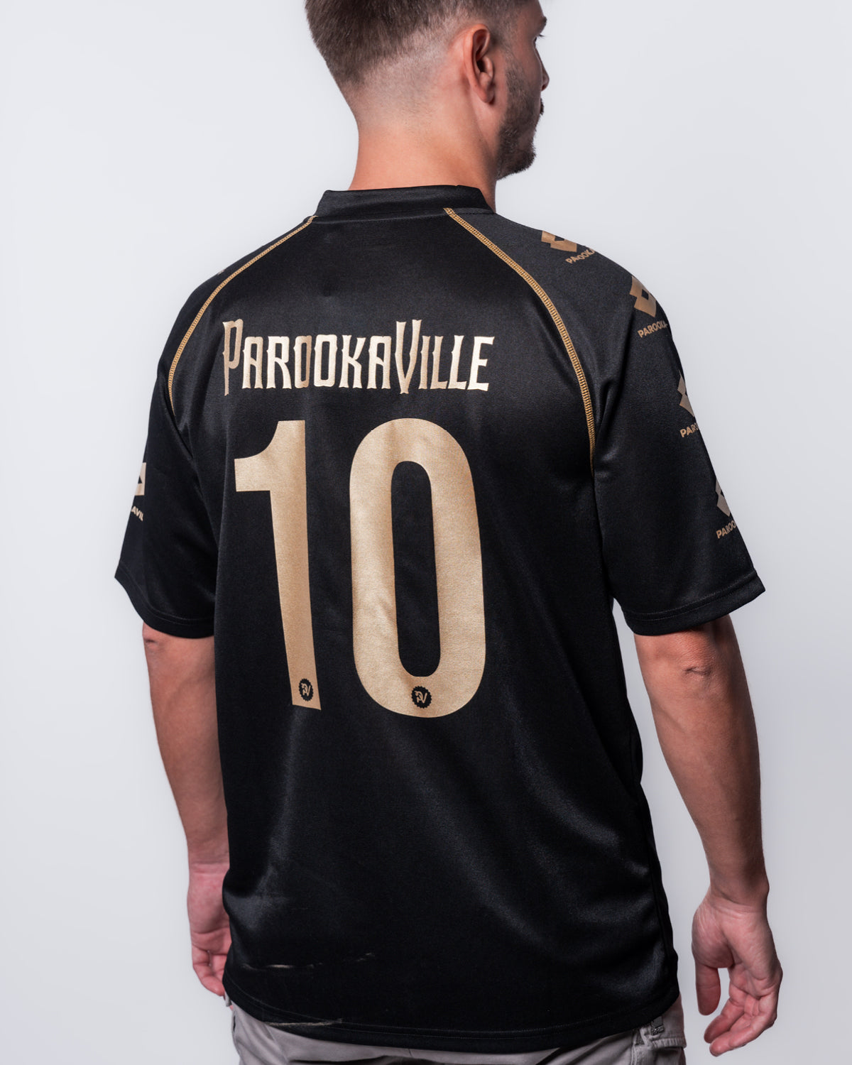 (DE) Eine Mann trägt das schwarze PAROOKAVILLE 10 Years Trikot. Man sieht sehr gut den Backprint "PAROOKAVILLE 10" in goldener Schrift. (EN) A man wears the black PAROOKAVILLE 10 Years jersey. You can clearly see the back print ‘PAROOKAVILLE 10’ in gold lettering.