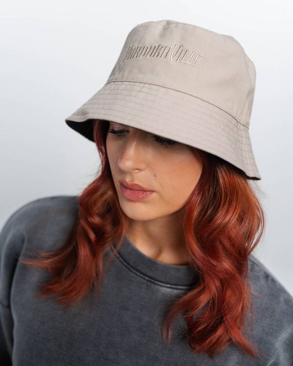 (DE) Eine Frau trägt einen dunkelgrauen Pullover mit der dunkelgrauer PV Aufschrift . Außerdem trägt sie einen beigefarbenen Bucket Hat . (EN) A woman is wearing a dark grey jumper with the dark grey PV inscription . She is also wearing a beige-coloured bucket hat .