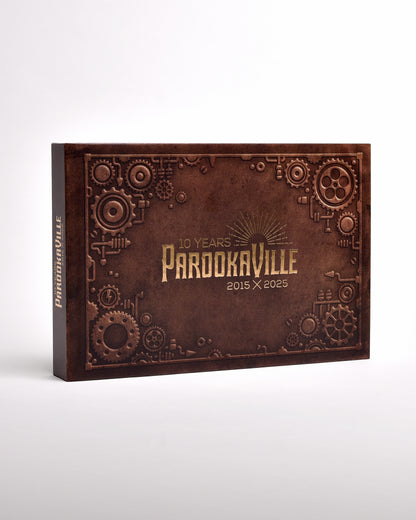 Zu sehen ist die Hülle des Buches im senkrecht-länglichen Format. Sie ist im Stil eines braunen Koffers mit goldenen Ecken gedruckt. Auf dem "Koffer" sind Sticker geklebt. Hier steht ein Sticker für eine Bühne der letzten 10 Jahre.