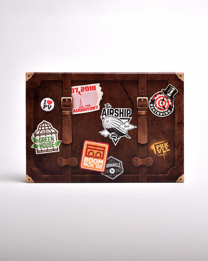 Zu sehen ist die Hülle des Buches im senkrecht-länglichen Format, frontal fotografiert. Sie ist im Stil eines braunen Koffers mit goldenen Ecken gedruckt. Auf dem "Koffer" sind Aufdrucke die aussehen, als habe man Sticker auf Ihn geklebt. Hier steht ein Sticker für eine Bühne der letzten 10 Jahre.