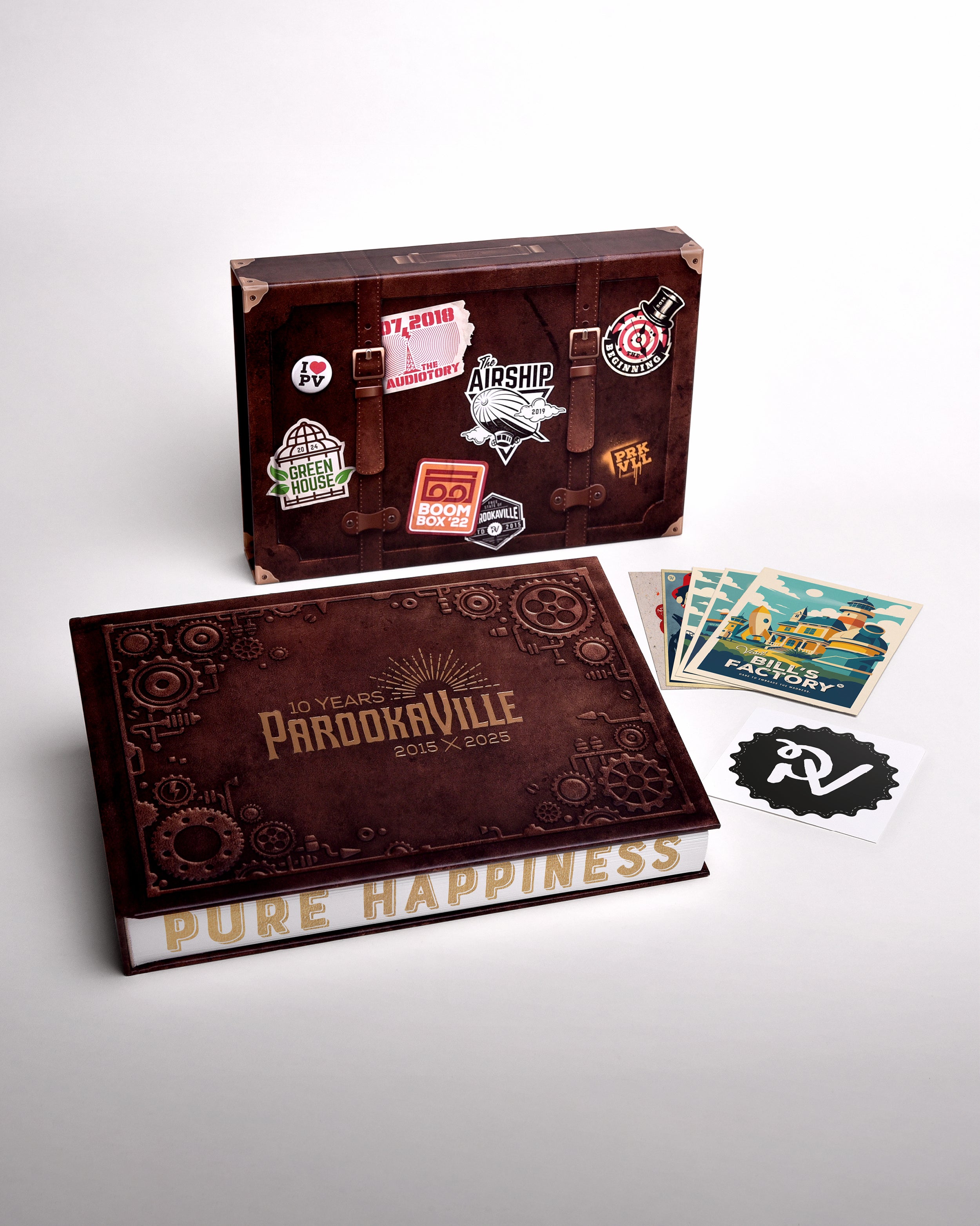 Zu sehen ist der gesamte Inhalt, der mit dem Buch geliefert wird. Das Buch, dessen Hülle, vier Parookaville Postkarten und ein Parookaville-Logo Sticker.