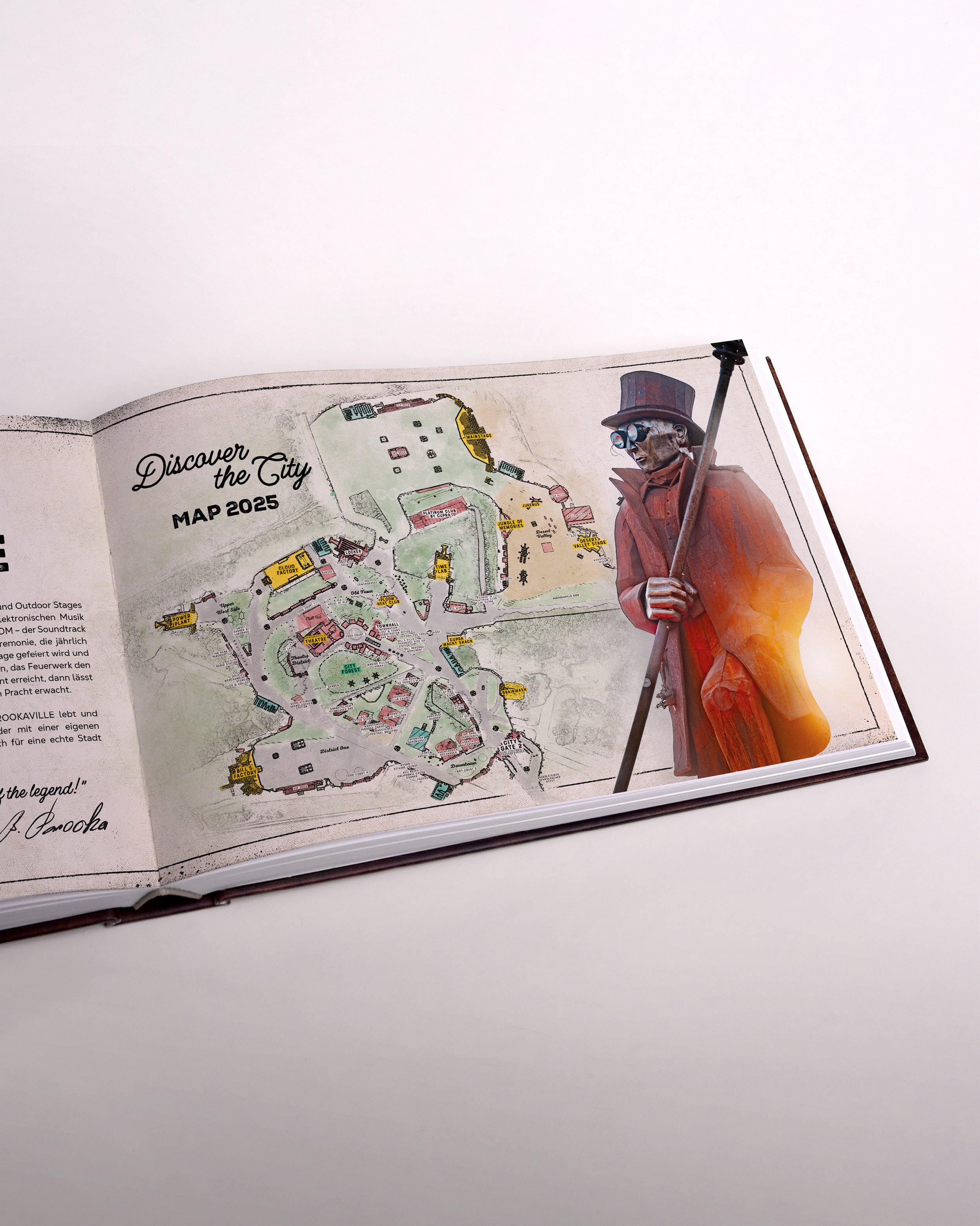 Zu sehen ist eine Seite des Buches im senkrecht-länglichen Format. Die Seite  zeigt die City-Map 2025. Daneben ist die Statue von Bill Parooka gedruckt. Sie schaut Richtung Karte.