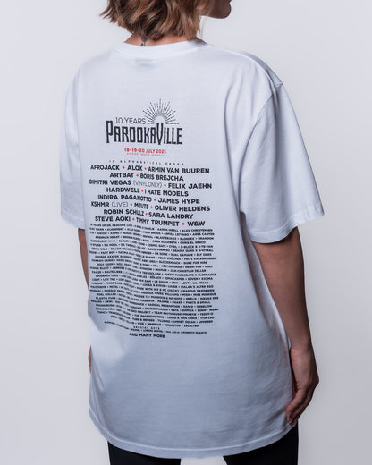 (DE) Eine Frau trägt ein weißes T-Shirt mit Line-Up Backprint und dem 10 YEARS PAROOKAVILLE Logo. (EN) A woman wears a white T-shirt with a line-up backprint and the 10 YEARS PAROOKAVILLE logo.